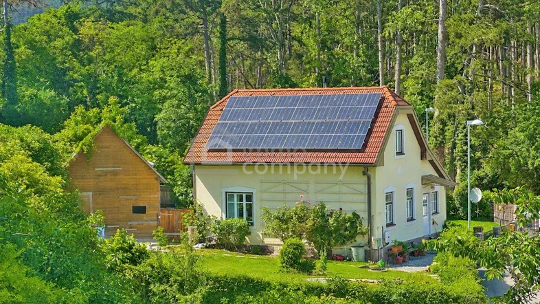 Landhaus mit Photovoltaikanlage auf dem Dach, umgeben von üppiger grüner Natur und Wald.