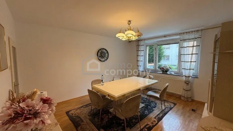 Helles Esszimmer mit modernem Esstisch, Holzfußboden und Fenster mit Blick ins Grüne.