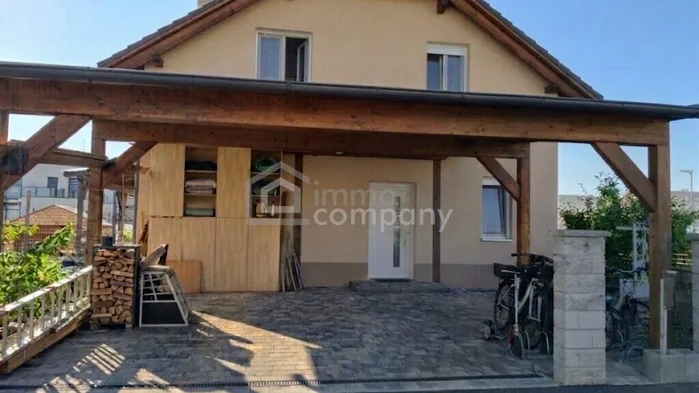 Vorderansicht eines Einfamilienhauses mit Holzcarport und gepflasterter Einfahrt.