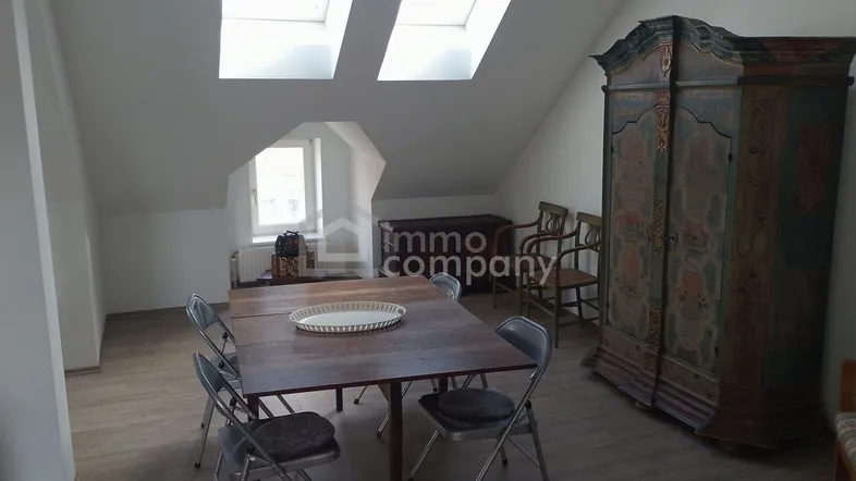 Geräumiger Essbereich im Dachgeschoss mit Holztisch, Stühlen und einem antiken Schrank unter Dachfenstern.