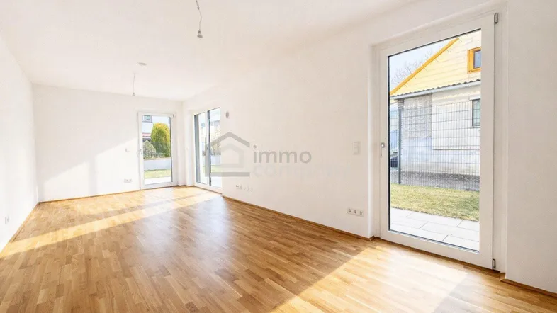 Helles, leeres Wohnzimmer mit Parkettboden und Zugang zu einem Gartenbereich durch große Fenstertüren.