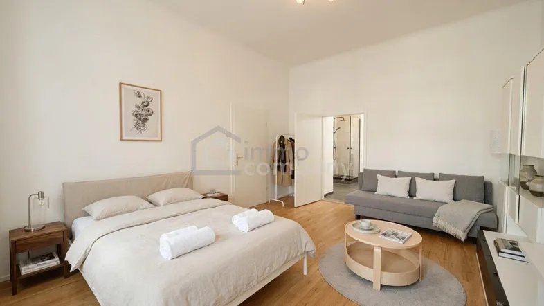 Helles Schlafzimmer mit Holzboden, einem bequemen Bett und einer kleinen Sitzecke mit Zugang zum Bad.