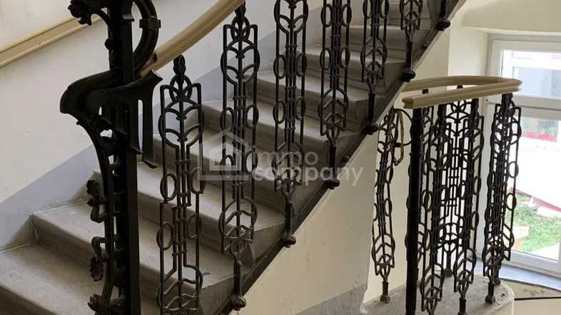 Historisches Treppenhaus mit kunstvollem schmiedeeisernem Geländer, Steinstufen und natürlichem Lichteinfall.