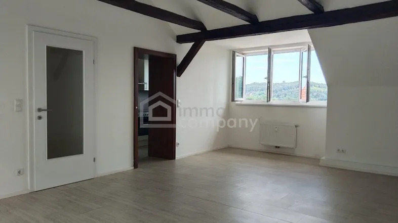 Helles Wohnzimmer im Dachgeschoss mit sichtbaren Holzbalken und Blick ins Grüne.