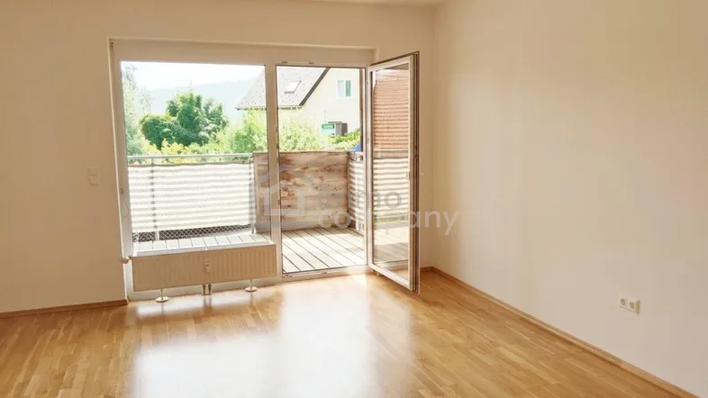 Helles Zimmer mit Holzboden und Zugang zu einem Balkon, ideal als Wohn- oder Schlafzimmer.