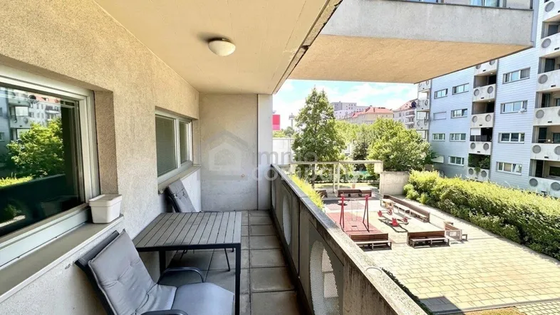 Geräumiger Balkon mit Sitzgelegenheiten und Blick auf den Innenhof mit Spielplatz.