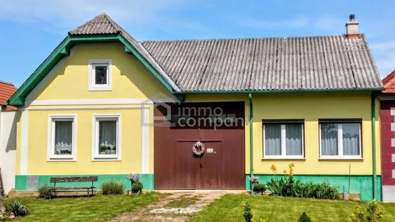 Traditionelles Landhaus mit gelber Fassade, grünem Dachgiebel und großem Holztor.