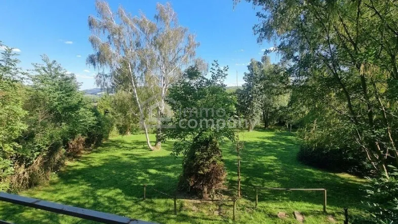 Panoramablick von einem Balkon auf einen weitläufigen, grünen Garten mit verschiedenen Bäumen und Sträuchern.