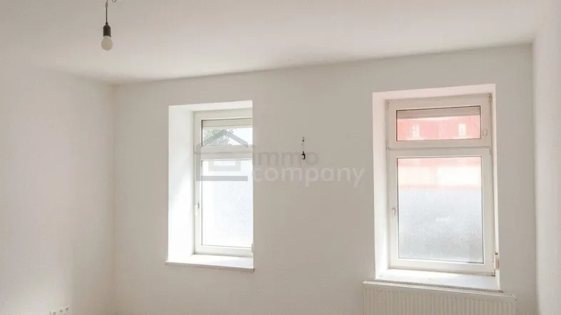 Helles, leeres Zimmer mit Laminatboden und zwei Fenstern, bereit zur individuellen Gestaltung.