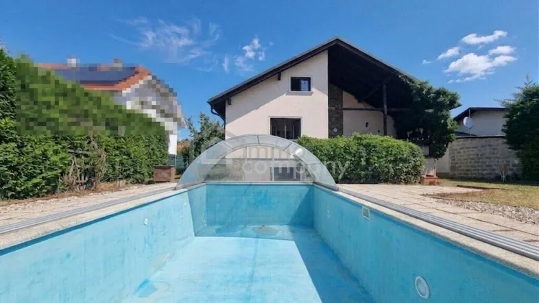 Leeres Schwimmbecken mit Abdeckung und Blick auf das Haus unter blauem Himmel.