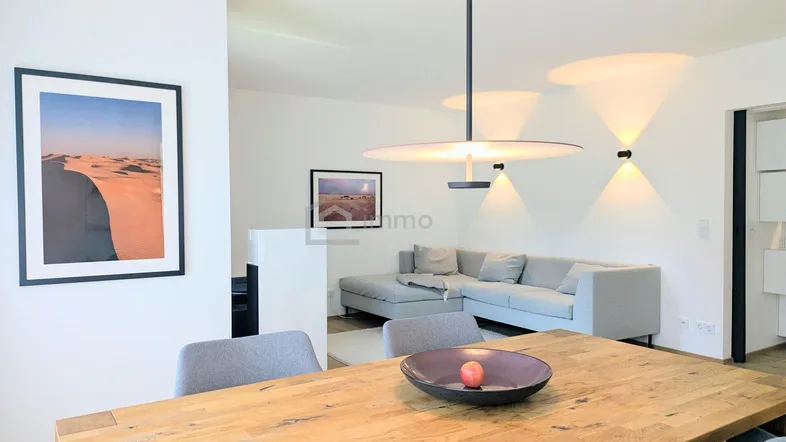 Moderner offener Wohn- und Essbereich mit Holztisch und bequemer Couch in hellem Ambiente.