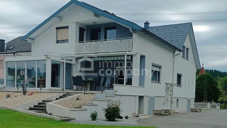Modernes Einfamilienhaus mit Wintergarten, Terrasse und Balkon unter bewölktem Himmel.