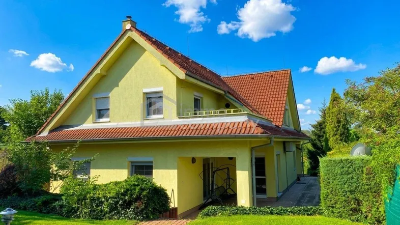 Gelbes Einfamilienhaus mit rotem Ziegeldach, umgeben von einem gepflegten Garten unter blauem Himmel.