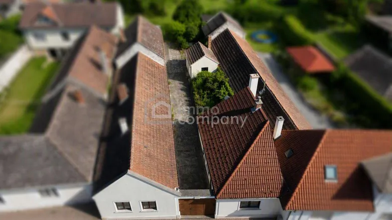 Luftaufnahme mehrerer Gebäude mit roten Ziegeldächern und einem schmalen Innenhof.