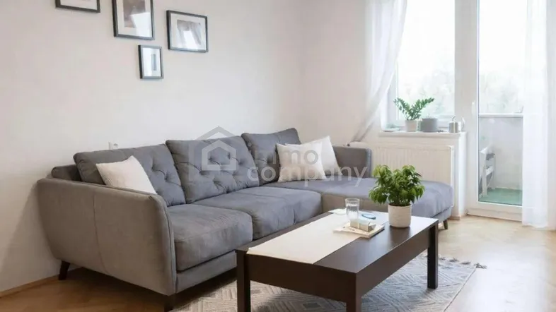 Helles Wohnzimmer mit einem bequemen grauen Ecksofa, Holzboden und Zugang zu einem kleinen Balkon.