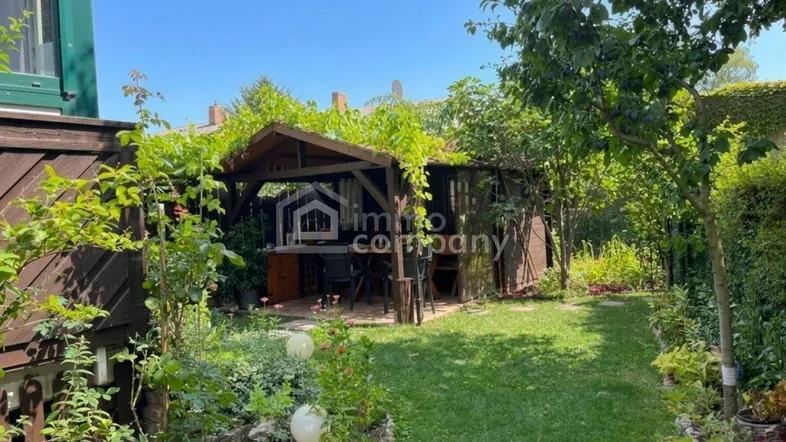 Gepflegter Garten mit Rasenfläche, Sträuchern und einem gemütlichen Holzpavillon im Hintergrund.