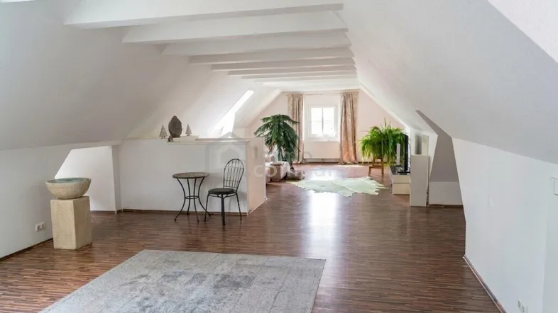Heller, offener Dachbodenraum mit sichtbaren Holzbalken, Schrägdach und Laminatboden.