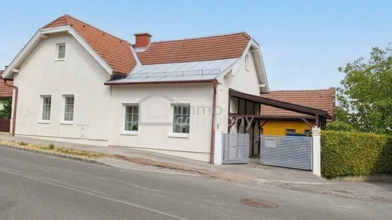 Weißes Einfamilienhaus mit Satteldach und Carport, von der Straße aus gesehen.