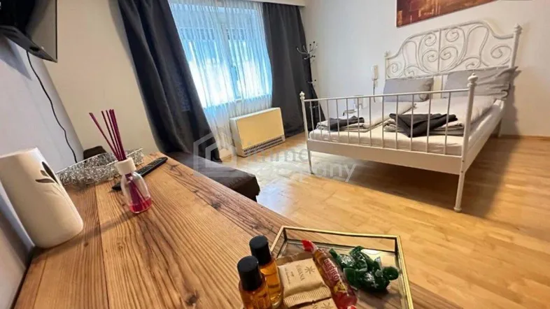 Helles Schlafzimmer mit Holzboden, weißem Metallbett und einem Schreibtisch am Fenster.