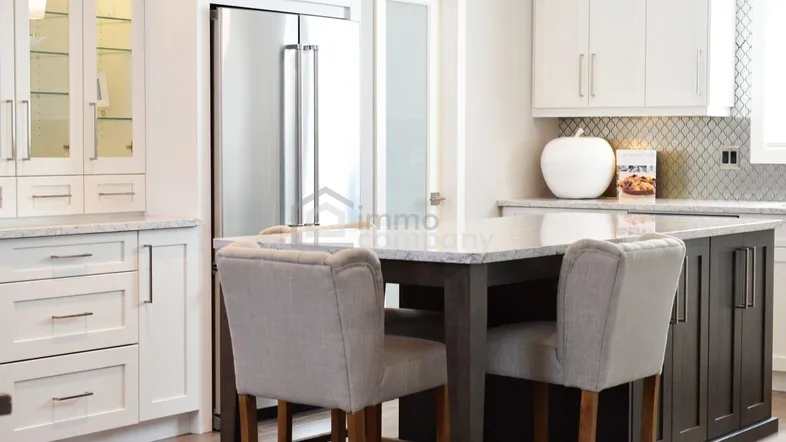 Moderne Küche mit Kücheninsel, Barhockern, weißen Schränken und einem integrierten Edelstahlkühlschrank.