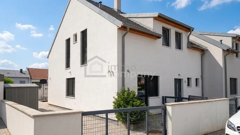 Moderne Doppelhaushälfte mit weißer Fassade, dunklen Fenstern und einem gepflegten Vorgartenbereich.
