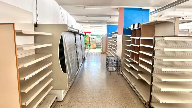 Gang in einem leeren Supermarkt mit Kühlregalen und Terrazzoboden, gut beleuchtet.