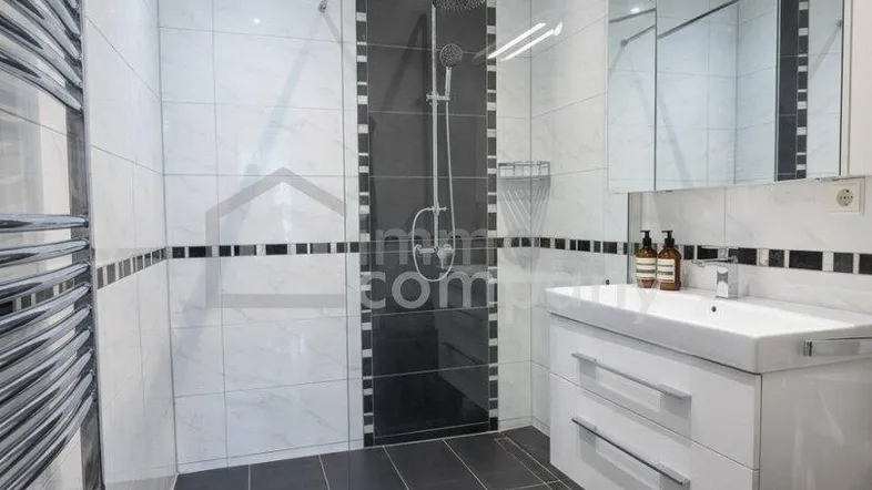 Modernes Badezimmer mit ebenerdiger Dusche, weißen und grauen Fliesen sowie einem Handtuchheizkörper.