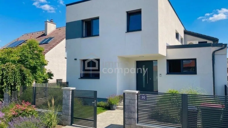 Moderne Einfamilienhausfassade mit klaren Linien, großen Fenstern und gepflegtem Vorgarten.
