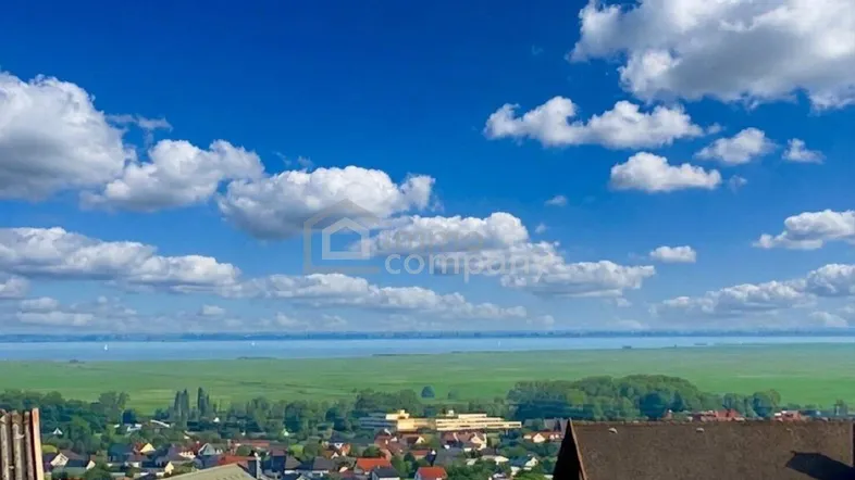 Weitläufiger Panoramablick über den See, grüne Felder und eine Stadt unter strahlend blauem Himmel.
