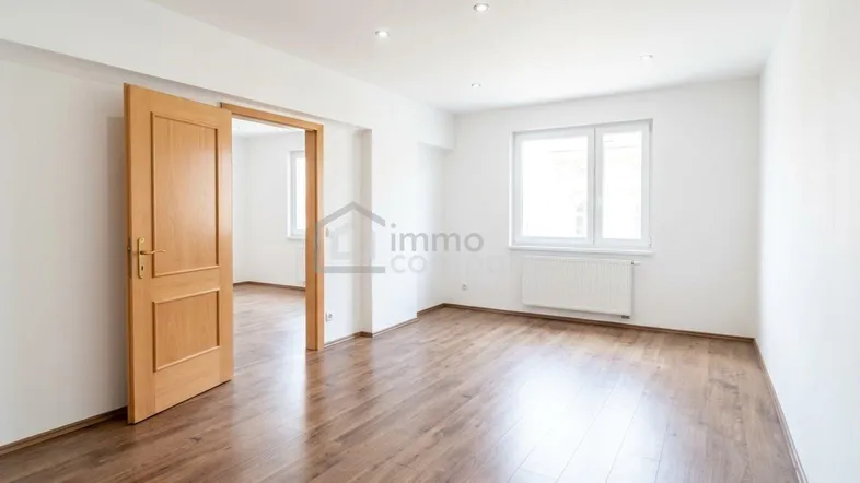 Helles Zimmer mit Holzboden, weißen Wänden und einem Fenster, das viel Tageslicht hereinlässt.