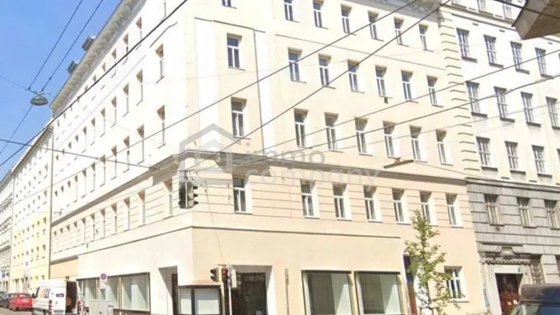 Mehrstöckiges Gebäude mit klassischer Fassade an einer belebten Stadtstraße mit Straßenbahnschienen und vielen Fenstern.