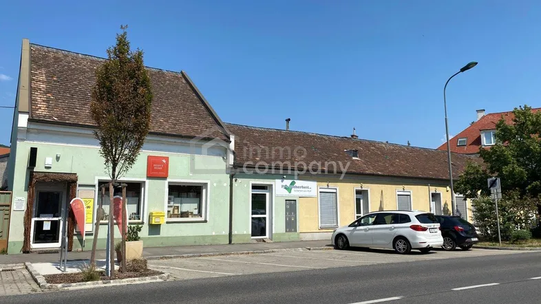 Gebäudeansicht mit verschiedenen Fassadenfarben, Parkplätzen und einer Straße im Vordergrund.
