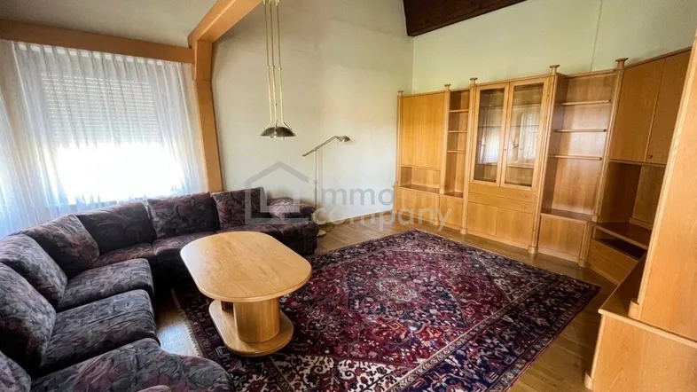 Gemütliches Wohnzimmer mit großem Sofa, Holzboden, traditionellem Teppich und Dachschräge.