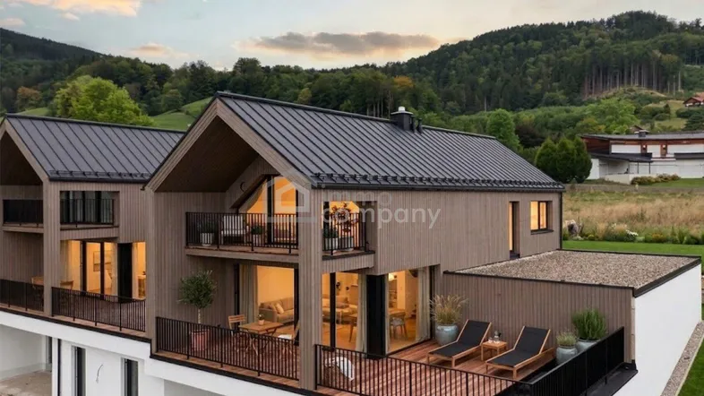 Moderne Häuser mit Holzfassade, Balkonen und einer möblierten Terrasse mit Bergblick.