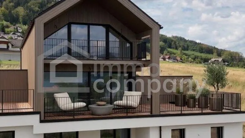 Moderne Architektur mit Balkonen und Terrasse, umgeben von grüner Landschaft.