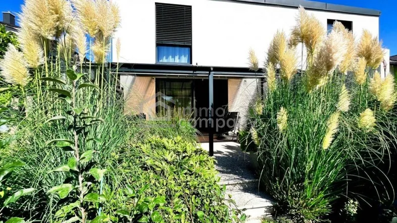Modernes Haus mit gepflegtem Garten und üppiger Bepflanzung, der zu einer Terrasse führt.