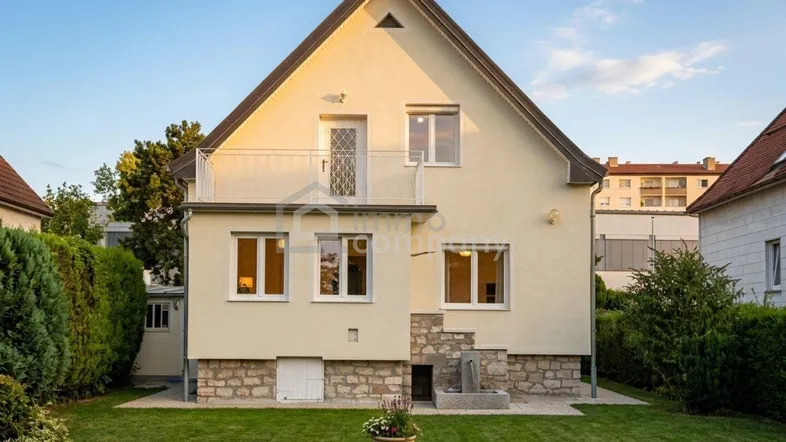 Rückansicht eines Einfamilienhauses mit Garten, Balkon und Steinfassade im unteren Bereich.