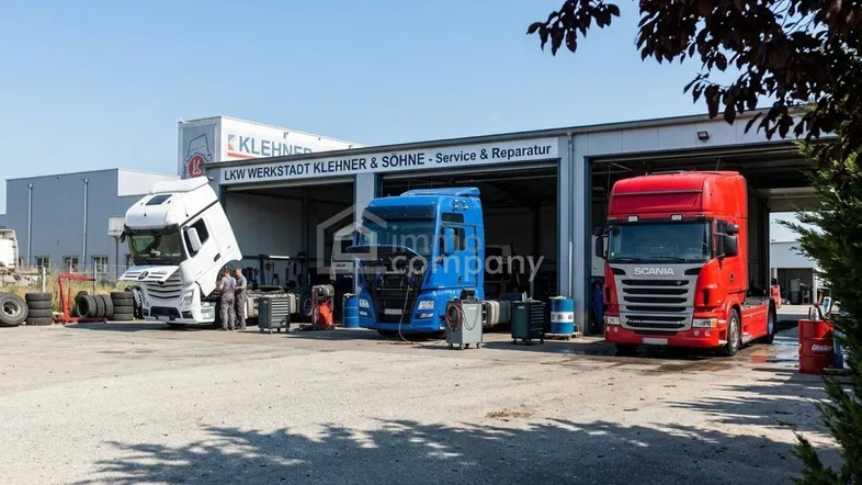 LKW-Werkstatt mit drei Lastwagen vor dem Gebäude unter blauem Himmel und Sonnenschein.