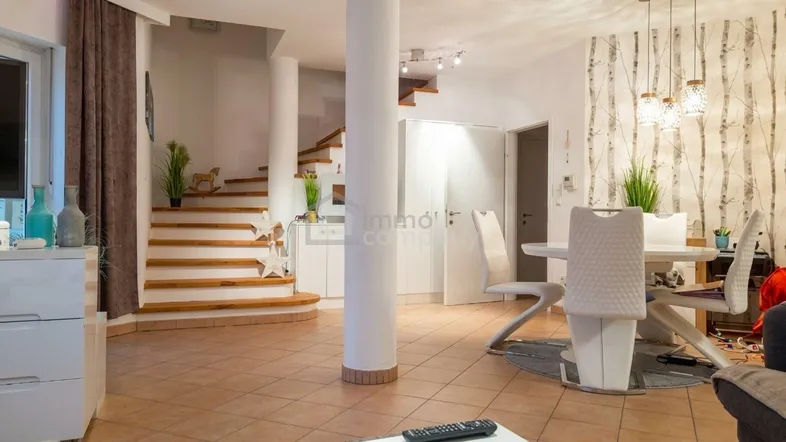 Heller Wohn- und Essbereich mit gefliestem Boden, moderner Einrichtung und offener Treppe.