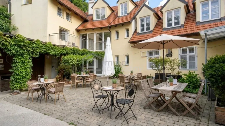 Gemütlicher Außenbereich mit Tischen, Stühlen und Sonnenschirmen, umgeben von traditionellen Gebäuden mit Efeu.