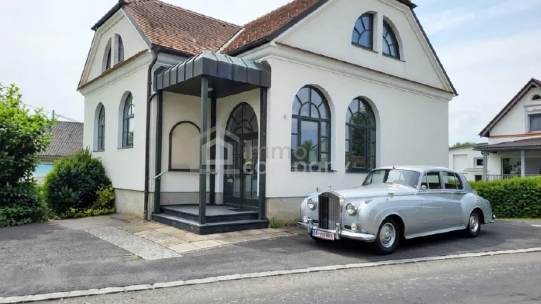 Weißes Haus mit markantem Eingangsbereich und einem Oldtimer davor auf der Auffahrt.