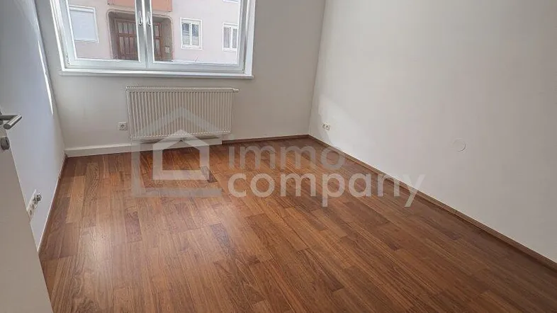 Helles Zimmer mit Holzfußboden und Blick auf die gegenüberliegende Fassade.