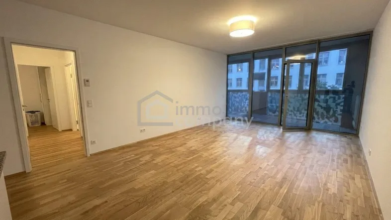 Helles, leeres Wohnzimmer mit Parkettboden und großen Fenstern, die Zugang zu einem Außenbereich bieten.