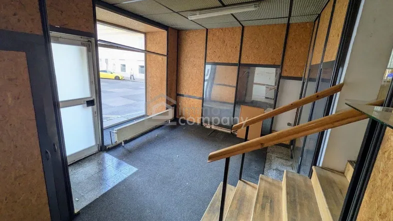 Eingangsbereich mit Treppe, großen Fenstern und Wänden aus Holzspanplatten, bietet viel Tageslicht.