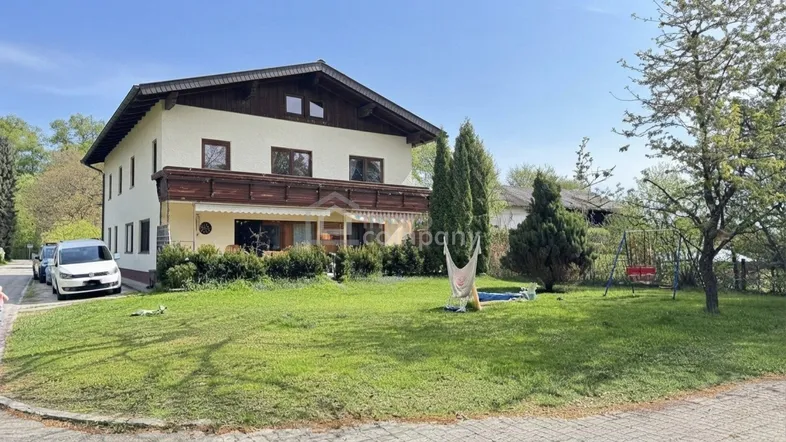 Haus im alpenländischen Stil mit großem Garten und Spielbereich im Freien unter blauem Himmel.