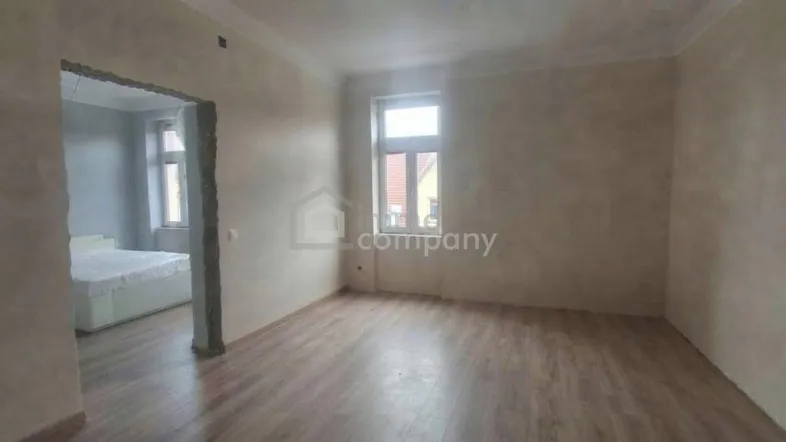 Heller Wohnraum mit Laminatboden und hohen Decken, der Zugang zu einem angrenzenden Schlafzimmer bietet.