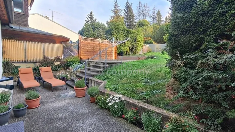 Gemütliche Terrasse mit Sonnenliegen und angrenzendem Gartenbereich, umgeben von viel Grün.