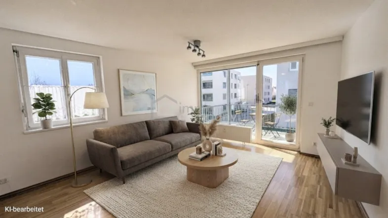Helles Wohnzimmer mit modernem Sofa, Holzboden und Zugang zu einem Balkon mit Blick auf umliegende Gebäude.