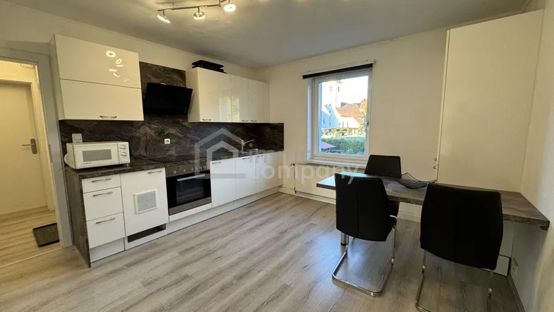 Moderne Einbauküche mit weißen Hochglanzfronten, dunkler Arbeitsplatte und integriertem Essbereich.
