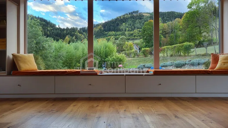Heller Raum mit großer Fensterfront und integrierter Sitzbank, die einen weiten Blick auf die grüne Landschaft bietet.